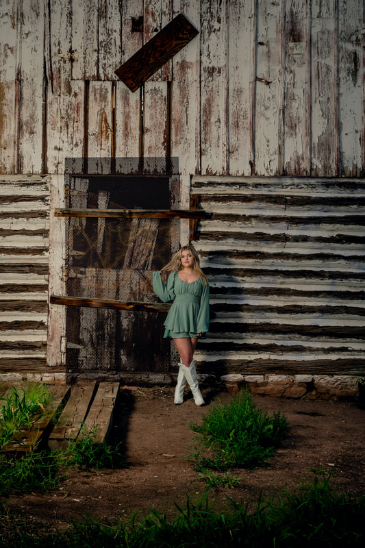 Girl in green dress standing in front of barn for senior pictures during golden hour parker colorado