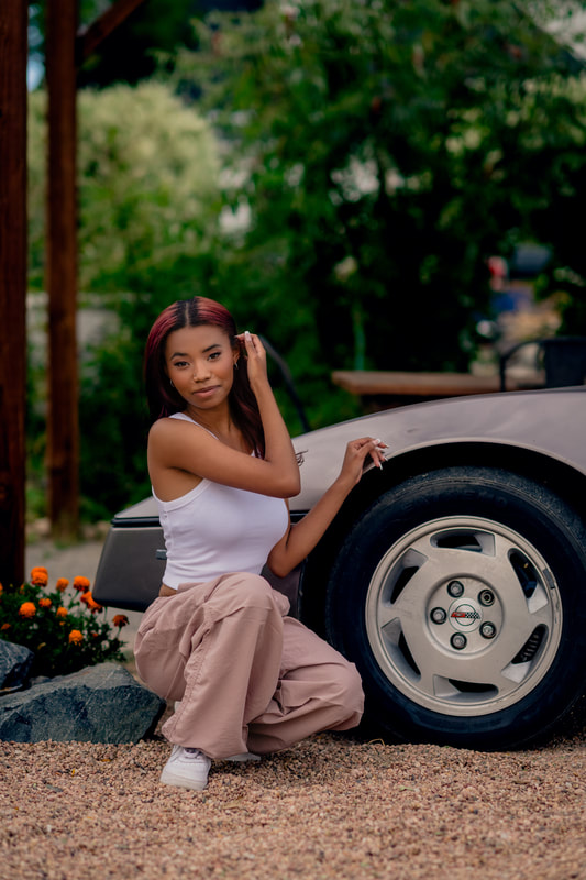 Girl in tan pants and white shirt sitting next to car senior photos broomfield colorado