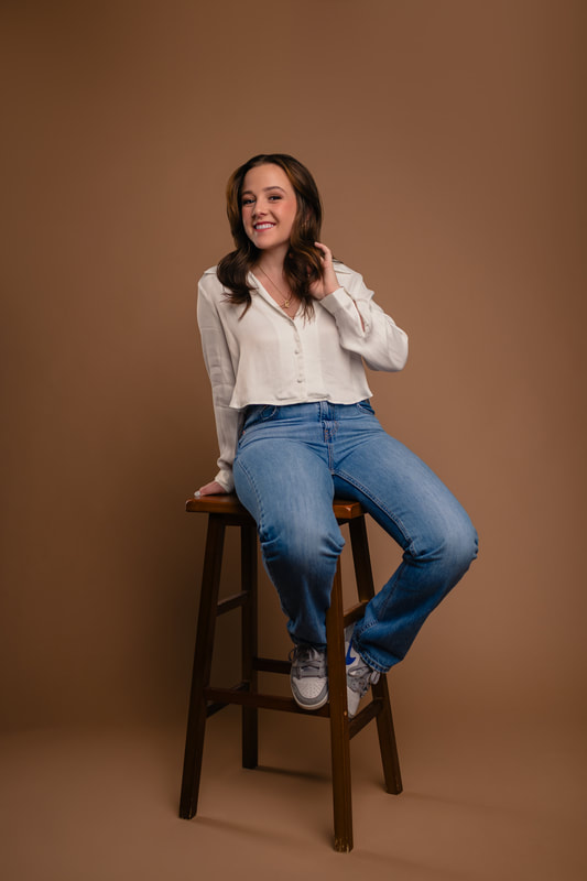 Girl in white shirt blue jeans and sneakers on stool in studio senior photoshoot parker colorado sarah lindsay photography