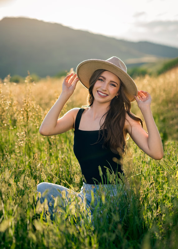 girl in black shirt and blue jeans in a field during sunset senior photoshoot in golden colorado 