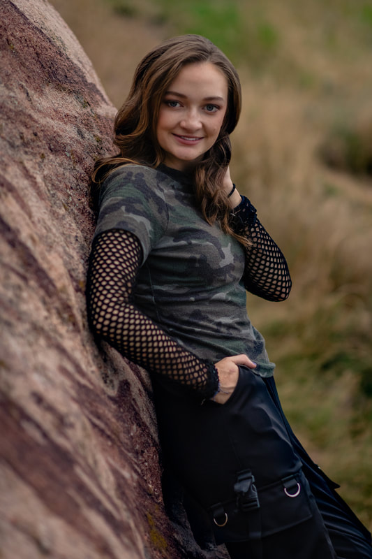 A girl in camo and black pants leaning on a rock in golden colorado senior pictures