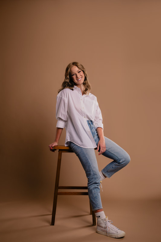 Girl in white shirt blue jeans and sneakers on stool in studio senior photoshoot parker colorado sarah lindsay photography