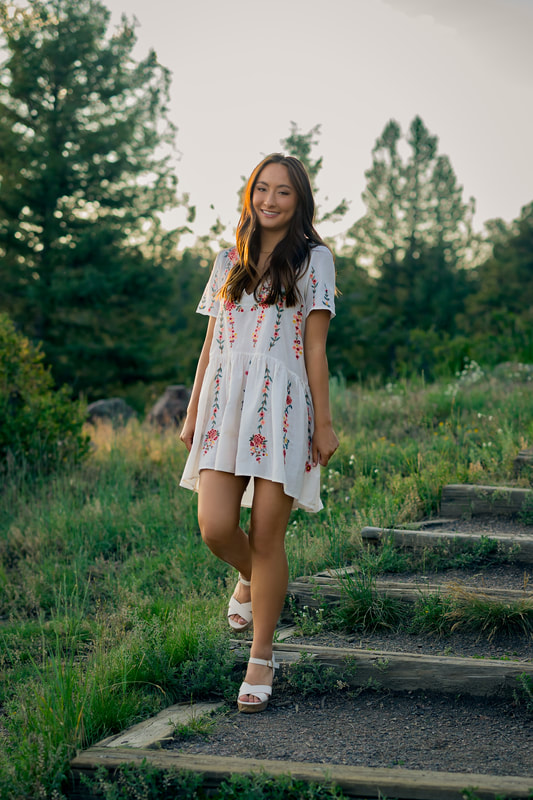 Girl in white dress walking in a field senior pictures during golden hour rocky mountains